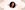A photo of a woman with brown hair is in a circle frame in the middle of the image. On all four corner and around the photo and around the frame there are green, pink, and yellow flowers. The background is a cream watercolor.